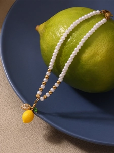 Close-up of lemon pendant and pearl necklace draped over a fresh lime and blue plate