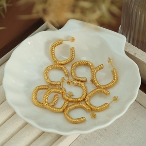 Golden C-shaped twisted hoop earrings displayed elegantly in a white shell-shaped dish