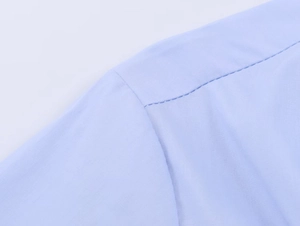 Macro detail of elastic poplin shirt stitching and light blue fabric texture on shoulder