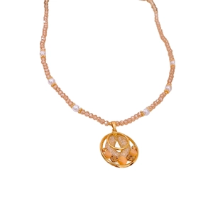 Collier en perles dorées élégant avec pendentif circulaire serti de zircons sur fond blanc