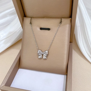 Close-up of a silver bow necklace on a white cushion inside a beige jewelry gift box