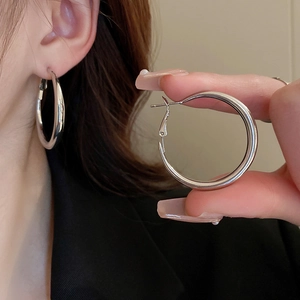 Detail view of large silver metal hoop earrings showing the secure clasp and polished finish
