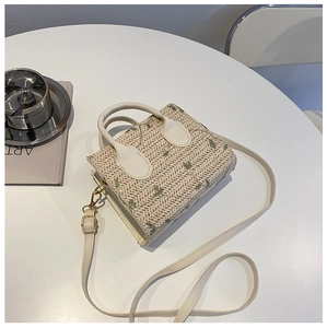Top view of a woven straw handbag with floral patterns and leather handles on a white table
