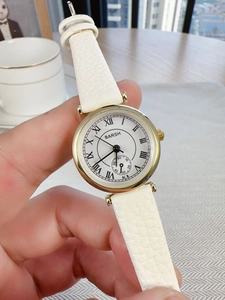 Detail of round gold quartz watch featuring Roman numerals and white textured leather strap