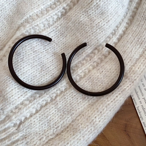 Close-up of minimalist black acrylic hoop earrings on white knit fabric background
