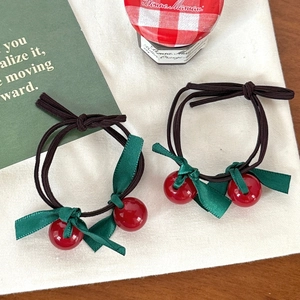 Detail of green ribbon bow hair ties with red cherry beads on white fabric