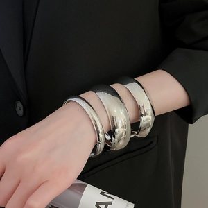 Gros plan sur trois bracelets joncs argentés avec une finition miroir polie