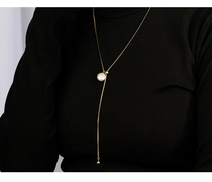 Detailed view of an adjustable gold Y-necklace with a baroque pearl on a black sweater