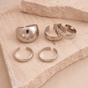 Macro detail of five-piece polished silver adjustable rings on beige stone pedestal