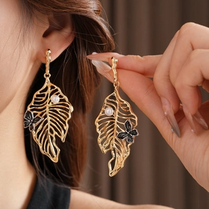 Detail of gold leaf earrings with pearl and black butterfly worn by a female model