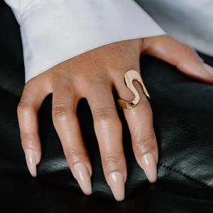 Close-up of a gold wavy stainless steel ring on black leather and white shirt cuff