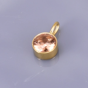 Golden round pendant with champagne crystal birthstone on a grey reflective background