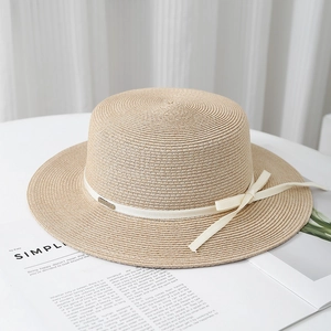 Detail of raffia sun hat with white bow ribbon and metallic logo plaque on magazines