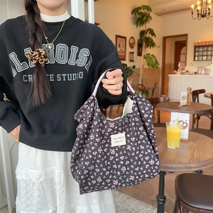 Detail of black floral knit handbag with pink handles held in a cozy cafe setting