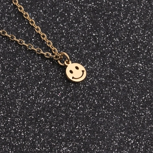 Dettaglio macro di un ciondolo a faccina sorridente dorato in acciaio su catena a O