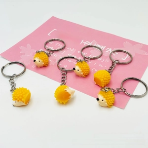 Close-up of six yellow resin hedgehog keychains with silver metal rings on white background