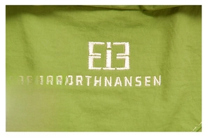 Detailed view of white NORTHNANSEN brand embroidery on grass green twill fabric backpack