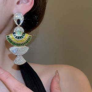 Close-up of gold layered fan earrings with green and yellow crystals on a model