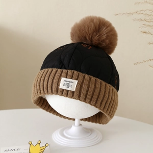 Détail du bonnet en maille avec grand pompon en fausse fourrure et écusson brodé élégant
