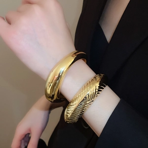 Gros plan détaillé de deux bracelets joncs dorés épais aux textures lisses et striées