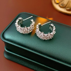 Macro shot of silver C-shaped earrings with zircon pavé on a dark green leather jewelry box