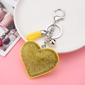 Sparkling gold heart keychain with yellow tassel and metal ball on white plate