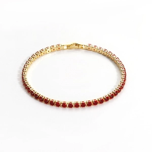 Detailed close-up of a gold tennis bracelet with red round cubic zirconia stones