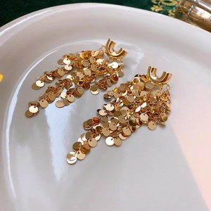 Close-up of gold layered sequin tassel earrings on white ceramic tray
