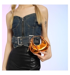 Detail of metallic orange crescent handbag featuring a high-gloss mirrored finish and handle
