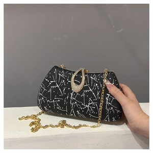Close-up of black evening clutch with white ink splatter pattern and gold diamond clasp