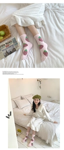 Close-up of pink coral fleece socks with strawberry pattern in a cozy bedroom setting