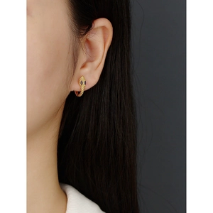Close-up of a gold snake hoop earring featuring blue gemstone eyes worn by a model