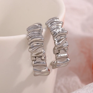 Detail of silver-plated C-shape earrings with vintage wrinkled texture on white ceramic