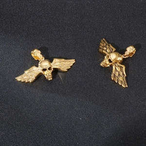 Gros plan de deux pendentifs crânes en acier titane doré avec ailes d'ange sur fond noir