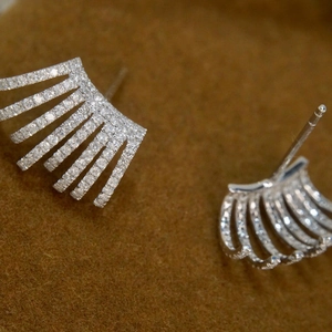 Macro shot of silver zircon stud earrings with multi-layered claw design on brown suede