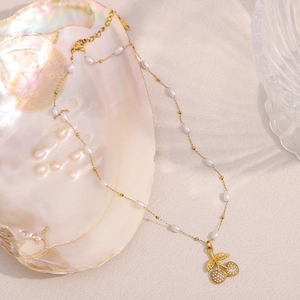 Detailed close-up of 18K gold-plated cherry pendant necklace with pearls inside a shell