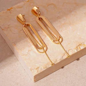 Close-up of golden double-layer geometric oval earrings on a marble stone background