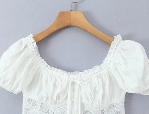Détail du haut en dentelle blanche avec manches bouffantes et motifs floraux fins