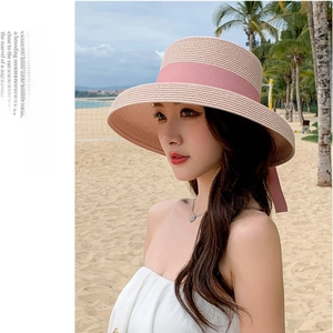 Detail of pink ribbon on a wide brim straw sun hat against a beach background