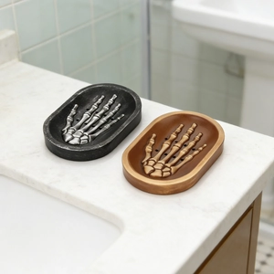 Detail of skull hand soap dishes in black and gold finishes on marble countertop