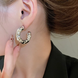 Detail of silver C-shaped hoop earrings with a hammered metal texture on a model