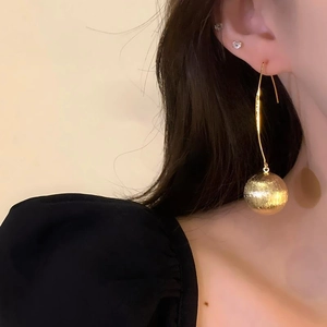 Elegant gold drop earrings with textured metal spheres worn by a model in a side view