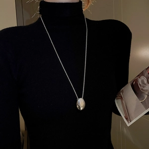 Detailed close-up of a silver oval pendant necklace worn over a black sweater