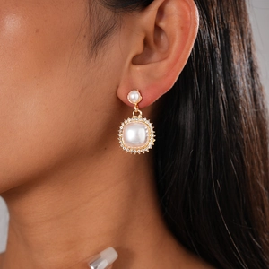 Close-up of elegant gold drop earrings with white pearls and sparkling zircon halo