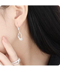 Close-up of irregular hollow silver earrings on model with high texture detail