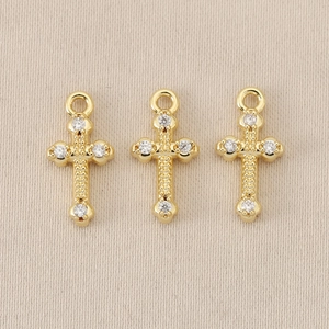 Macro view of gold plated 18K baroque cross charms with sparkling zircon stone inlays