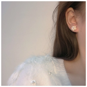 Detail of camellia earring featuring white enamel petals and central pearl on model