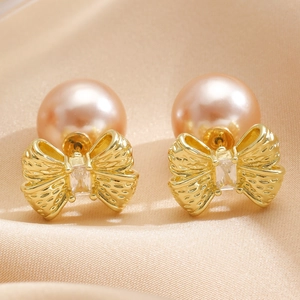 Macro detail of champagne pearl earrings with gold bow and sparkling zircon accents