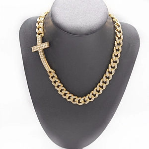 Macro shot of gold-plated iced out Cuban link chain with a cross pendant on a black bust