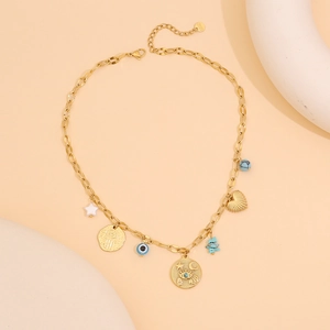 Détail du collier doré avec charms étoile, œil bleu et coquillage cœur sur fond beige